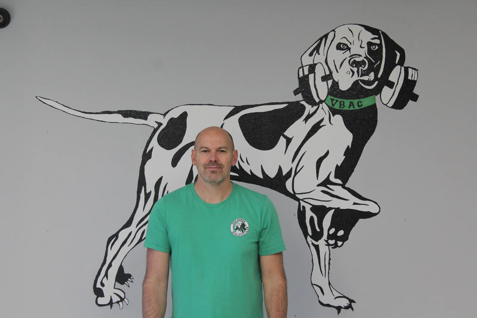 James Peck, owner of Van Buren Athletic Club, standing in front of the Pointer mascot mural